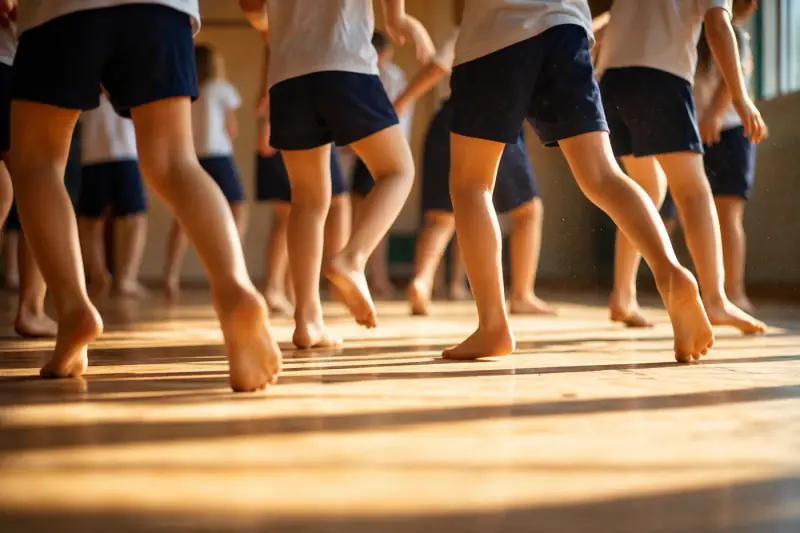 A line of pupils mid-step in a hall, weight low and knees bent, following a facilitator at the front.