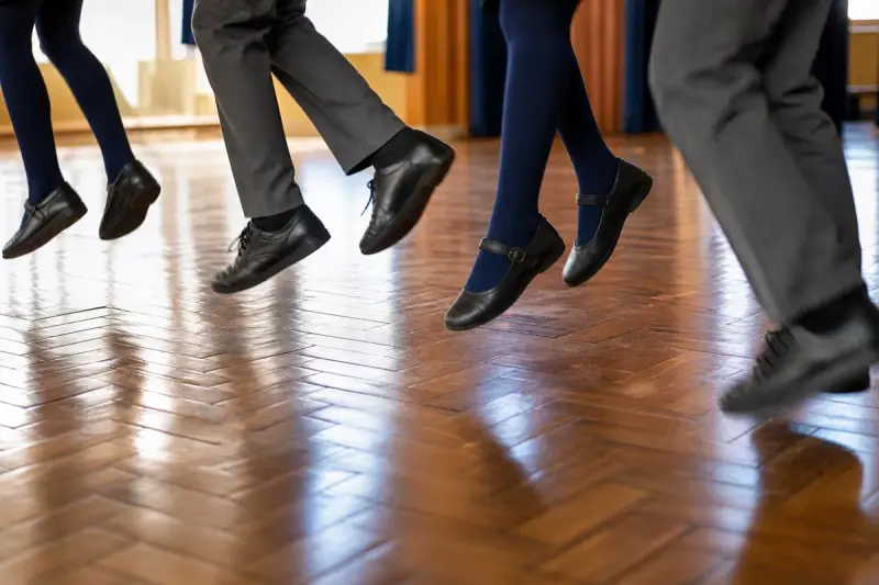 Close view of pupils' feet in plimsolls mid-sidestep on a hall floor, one foot crossing in front of the other.