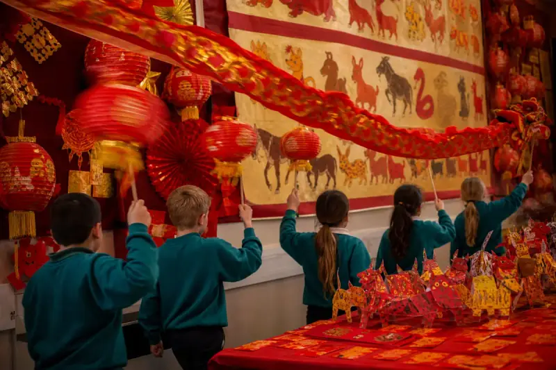 Red paper lanterns, gold-stamped red envelopes and a hand-painted zodiac scroll on a dark table.